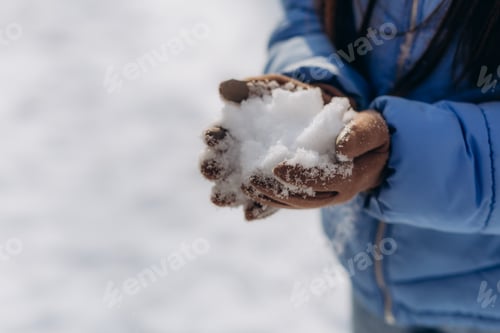 Preview: A young woman wearing mittens holds snow in her hands. close-up.