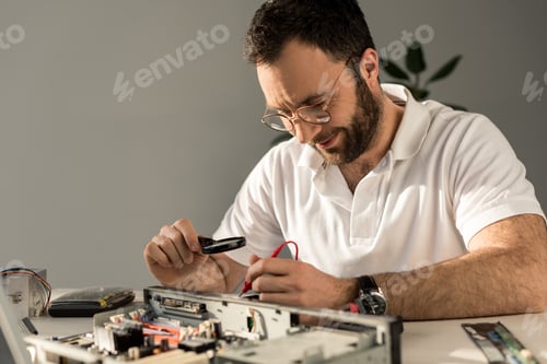 Preview: repairman using magnifier and multimeter while fixing pc