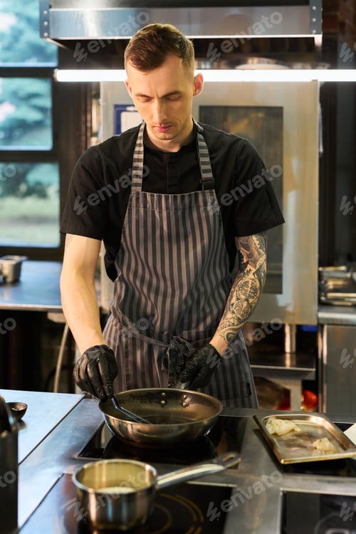 Preview: Young Adult Caucasian Man Cooking in Professional Kitchen Wearing Apron