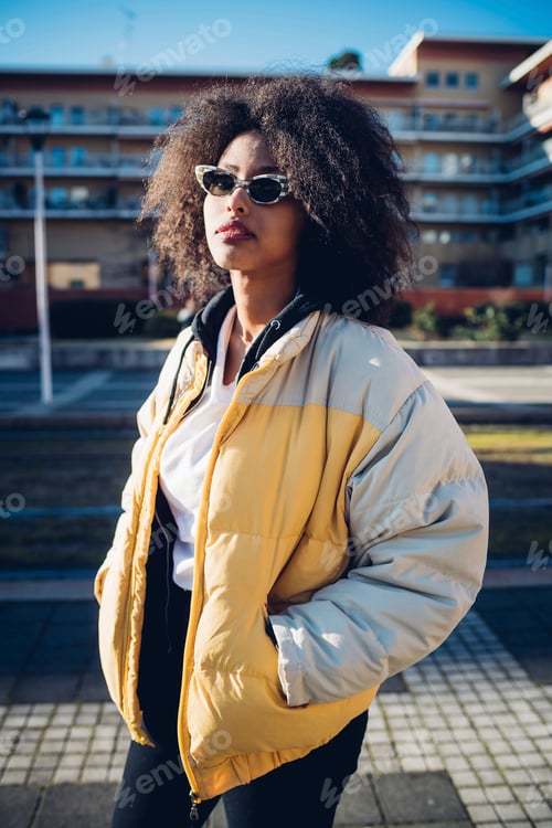Preview: Cool young woman wearing sunglasses on urban sidewalk, three quarter length portrait