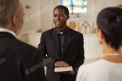 Preview: Smiling Black Priest Officiating Wedding in Church and Holding Bible