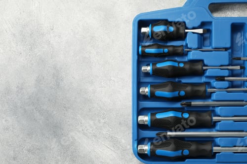 Preview: Set of screwdrivers in open toolbox on light grey textured table, top view. Space for text