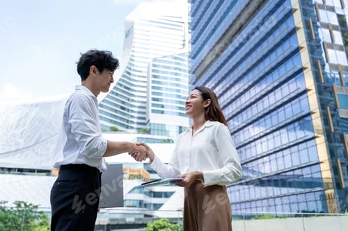 Preview: Asian businessman and businesswoman making handshake outdoors in city.