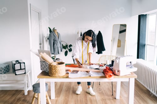 Preview: Young woman with sewing machine material laptop working at table