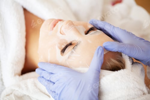 Preview: Beautiful young woman is applying a cosmetic tissue mask on a face
