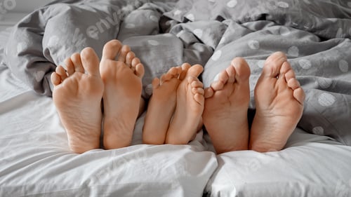 Preview: Parent's and child's feet playfully moving to the rhythm under the blanket on a cozy bed