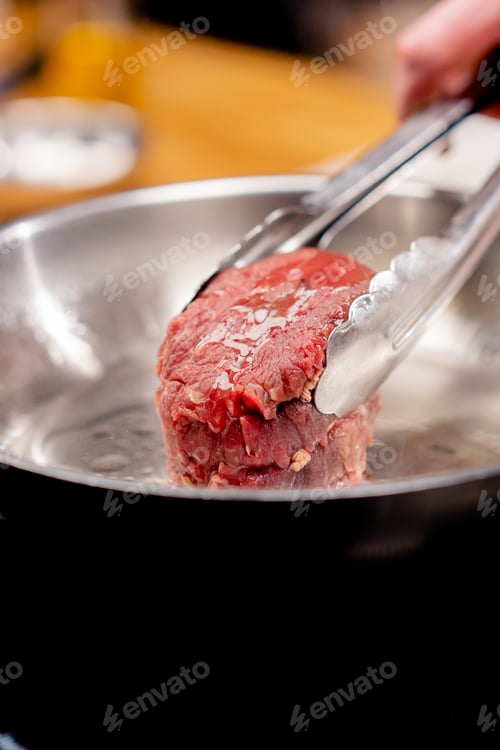 Preview: close-up in a professional kitchen with tongs holding a beef steak over hot frying pan with oil