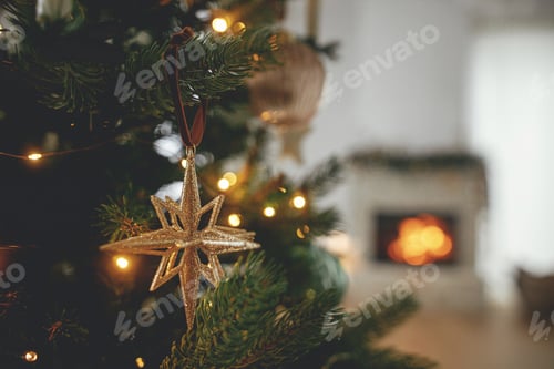 Preview: Merry Christmas! Stylish christmas gold star on tree close up against burning fireplace