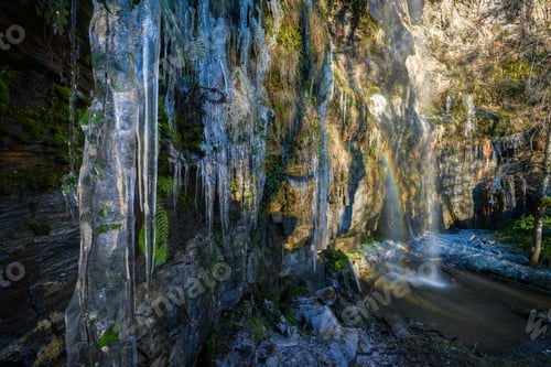 Preview: Frozen icicles on the cliff and a small rainbow on the waterfall