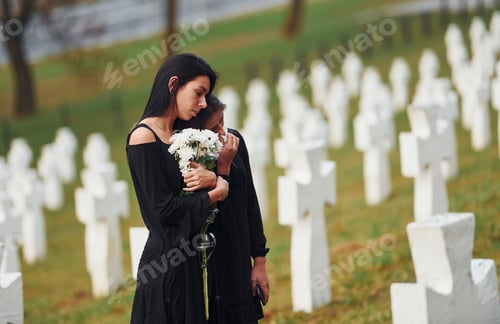 Preview: Two young women in black clothes visiting cemetery with many white crosses