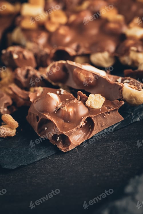 Preview: milk chocolate with nuts pieces on crumpled paper on gray surface