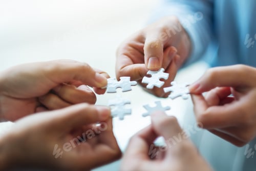 Preview: Closeup image of a group of people holding and putting a piece of white jigsaw puzzle together