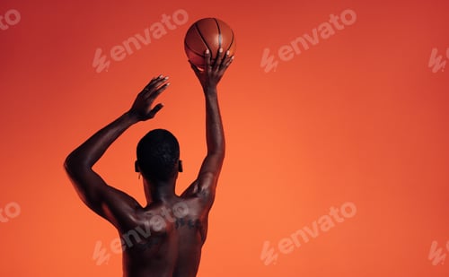 Preview: Rear view of a muscular athlete prepare to throw a basket ball in studio