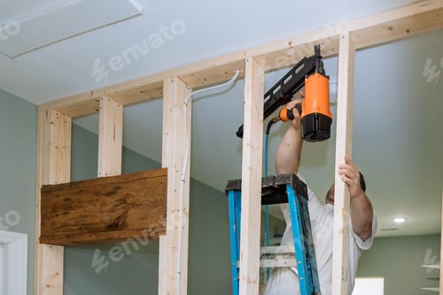 Preview: With help of an air hammer, builder nails wooden beams to frames of a house for construction