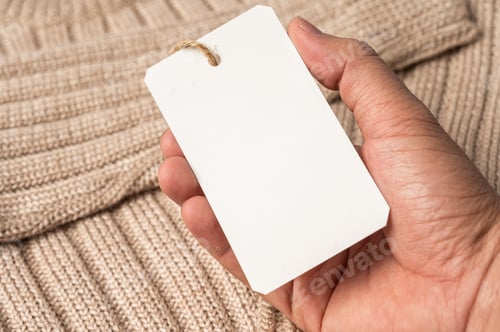 Preview: A hand holding a white tag on a brown sweater.