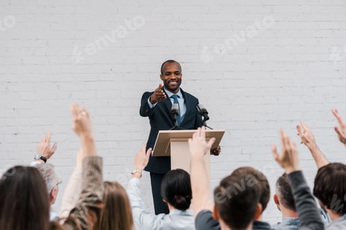 Preview: back view of journalists with raised hands near happy african american speaker gesturing near