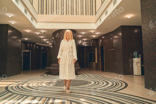 Preview: Woman wearing white soft bathrobe standing in the hall of spa hotel