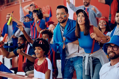 Preview: Young couple watching sports game with group of fans on a stadium.