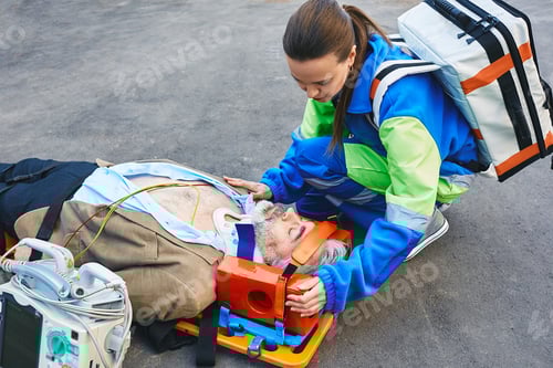 Preview: Female paramedic fixing head of male victim with neck injury lying on ambulance stretcher. First