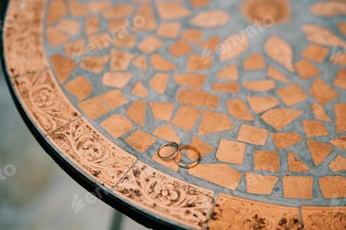 Preview: Wedding rings lie on a round mosaic table