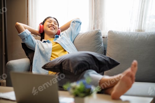 Preview: Happy asian woman listening to music while leaing back on couch.