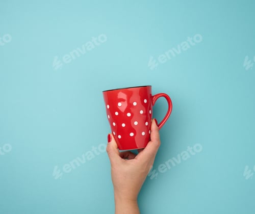 Preview: Female hand holding a red ceramic mug on a blue background, break time