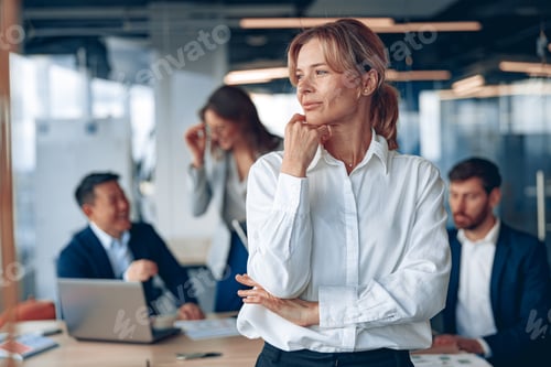 Preview: portrait of confident female boss looking at side with her colleagues at background in office