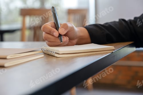 Preview: loseup image of a hand writing on blank notebook on table in cafe