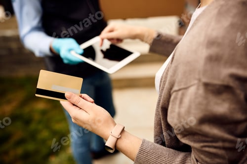 Preview: Close-up of woman paying with credit card while receiving home delivery.