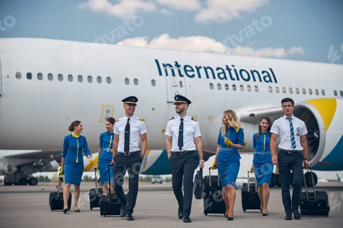 Preview: Cheerful aircrew with travel suitcases walking down the airfield