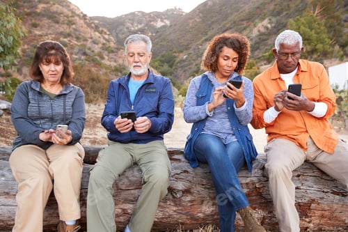 Preview: Group Of Senior Friends On Hike In Countryside Checking Mobiles Phones For Fear Of Missing Out