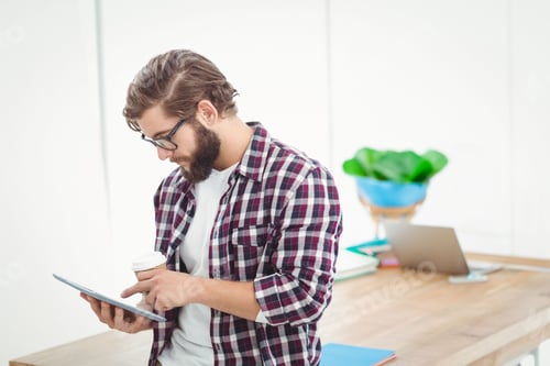 Preview: Holding coffee cup, man using tablet at office desk, with laptop and plant, copy space