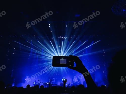 Preview: Silhouette of a hand holding up a phone in landscape mode in front of a disco ball at a concert