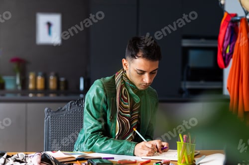Preview: Biracial transgender fashion designer sitting at desk and drawing sketches