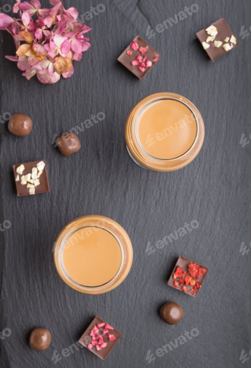 Preview: Sweet chocolate liqueur in glass with chocolate candies on a black stone slate board. Top view