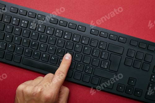 Preview: Cropped view of man pushing button on black computer keyboard on red background
