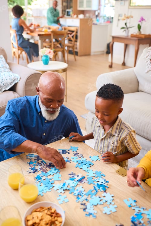 Preview: Grandparents With Grandchildren Indoors At Home Doing Jigsaw Puzzle With Parents In Background