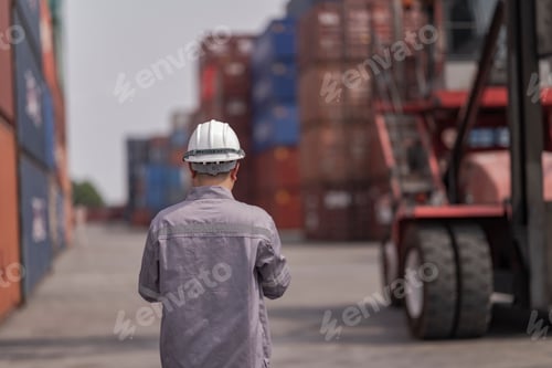 Preview: A logistics worker in a gray uniform inspects stacked shipping containers