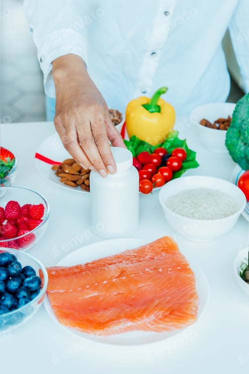 Preview: Focus on female hand putting white mockup jar with nutritional supplements on table with fresh food