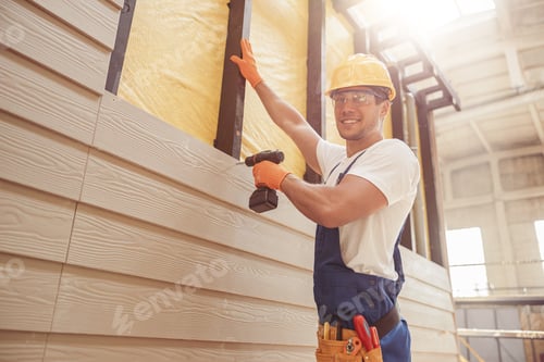 Preview: Cheerful builder using cordless electric drill at construction site