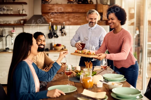 Preview: Happy African American Woman Serving Food While Having Meal With Her Friends At Home.