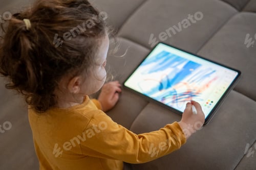 Preview: Top view little girl drawing on a digital tablet in a cozy living room.
