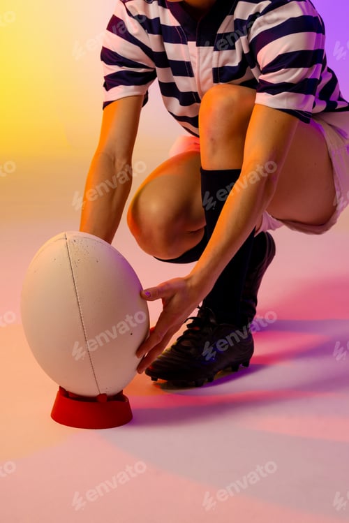 Preview: Caucasian female rugby player crouching with rugby ball over neon pink lighting