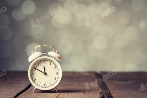 Preview: White alarm clock on wooden table with bokeh