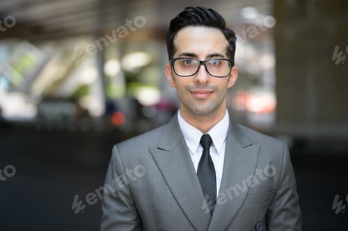 Preview: Face of young handsome Persian businessman in the city streets outdoors