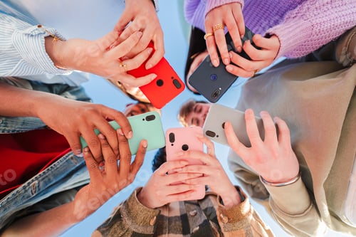 Preview: Low angle view of a group of unrecognizable multiracial young friends using their cellphones on a