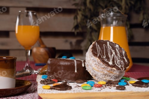 Preview: Shot of mini chocolate cakes with candies of different colors around and orange juice on the table