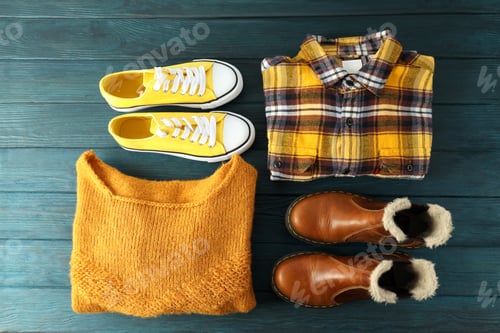 Preview: Shirt, sweater, sneakers and boots on wooden table