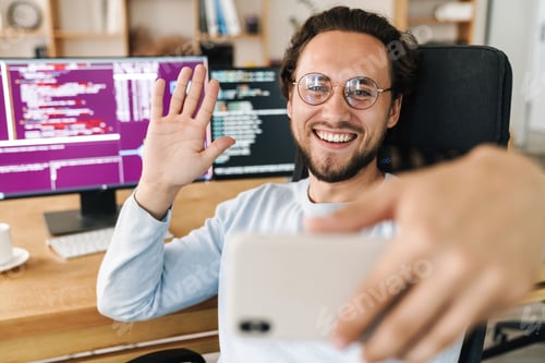 Preview: Image of programmer man waving hand while taking selfie on cellphone