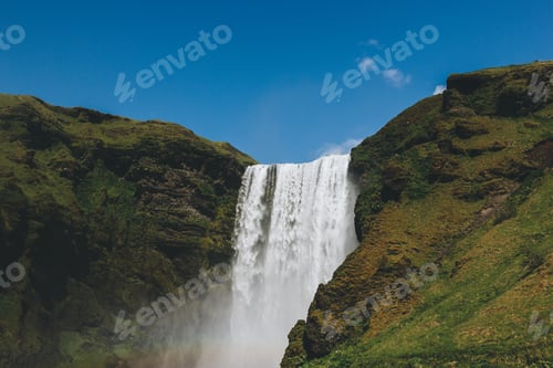 Preview: scenic view of waterfall Skogafoss against bright blue sky in Iceland